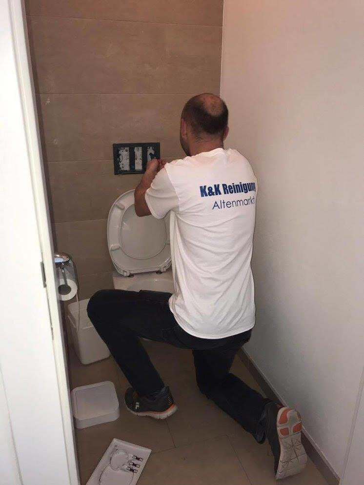 Mitarbeiter putzt eine Toilette